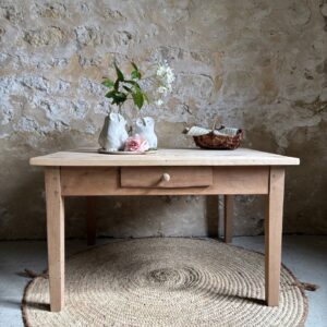 Table basse petit format en bois brut avec un tiroir central, style campagne chic posée sur un tapis rond en jute.